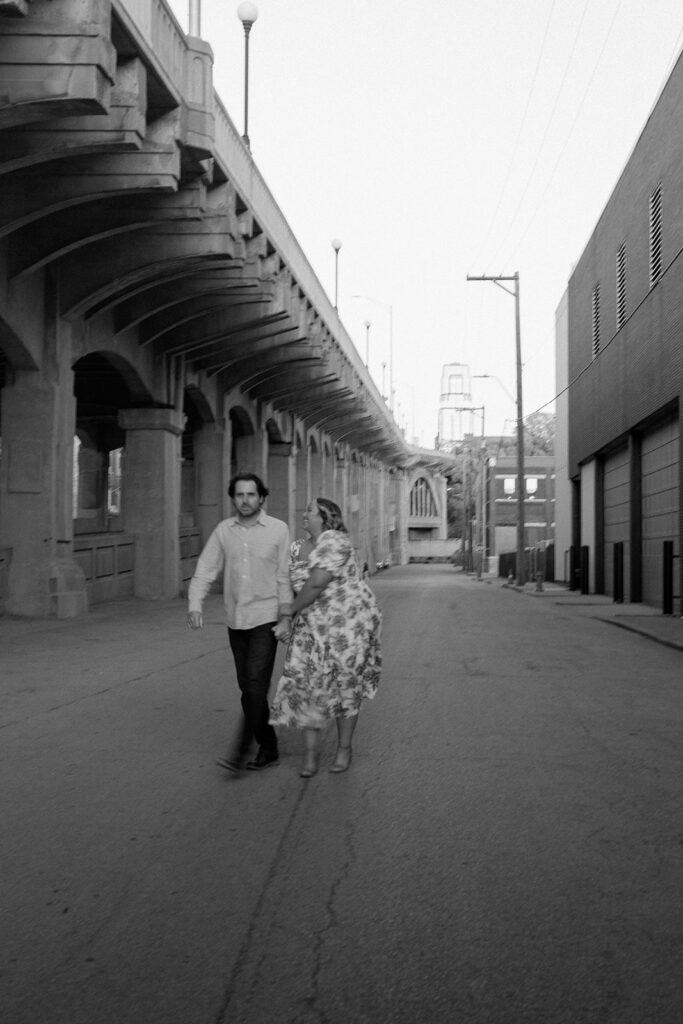 couple holding hands and walking under bridge