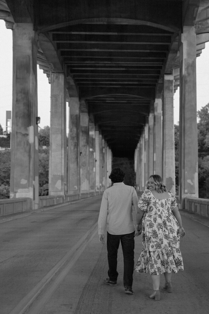 couple holding hands and walking under bridge