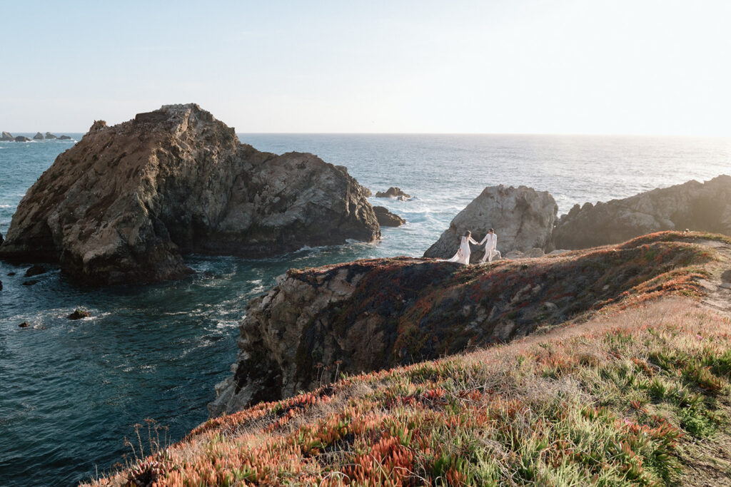 couple holding hands and walking in big sur off in the distance