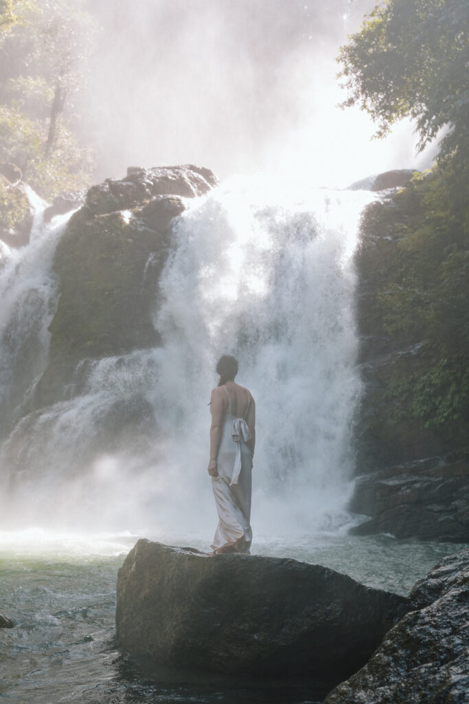 bride standing on rock in front of big waterfall