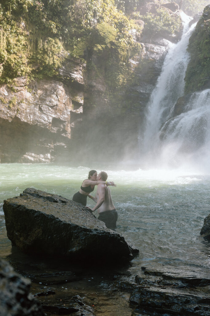 couple kissing pose in front of waterfall on rock