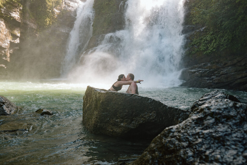 couple kissing on rock in front of waterfall for tropical adventure elopement