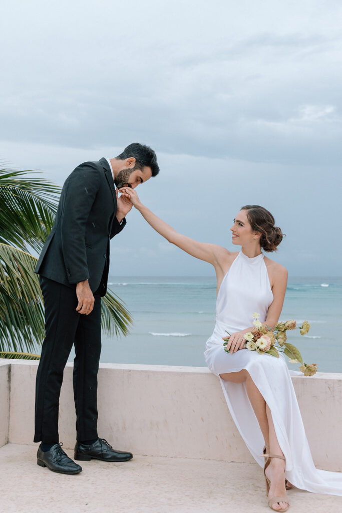 groom kissing brides hand on the beach