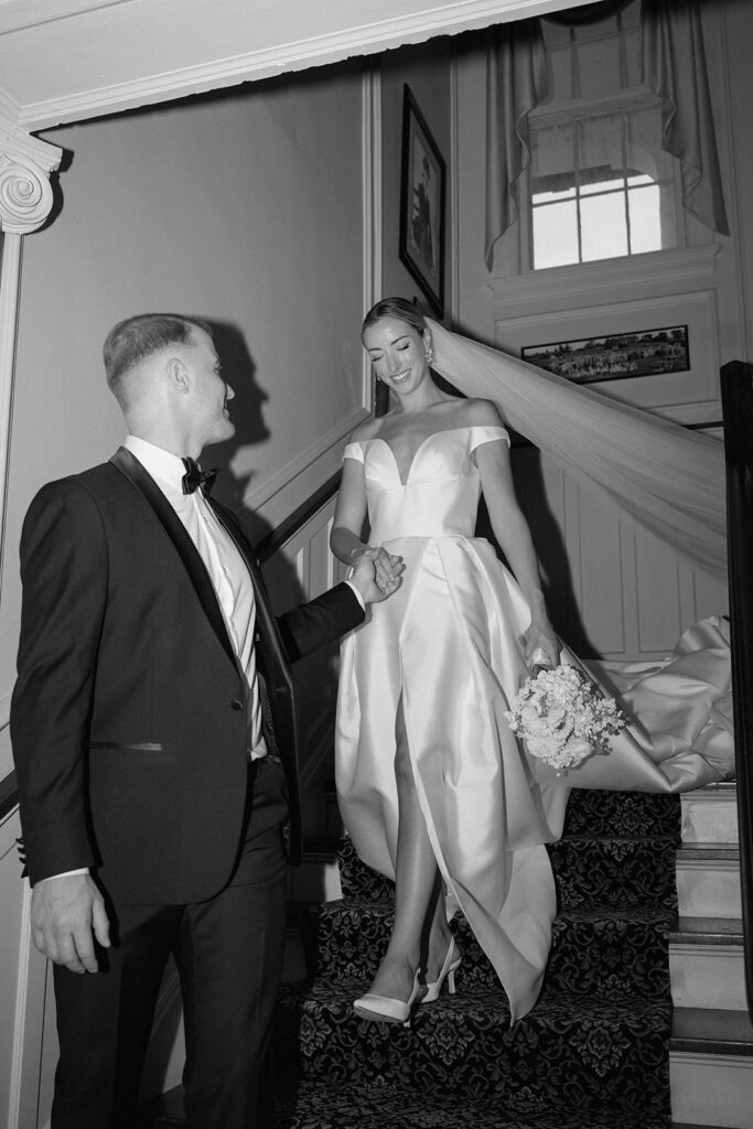 A black and white wedding photo of the model bride and groom walking down the grand staircase in Longview Mansion wedding venue.