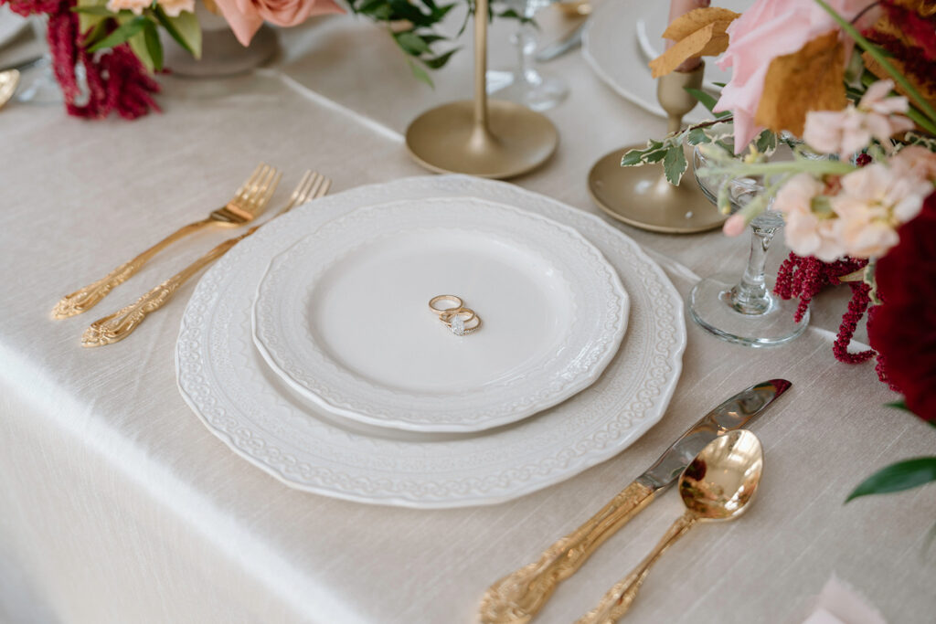 Wedding rings on Quest Events china with gold flatware for a styled wedding tablescape.