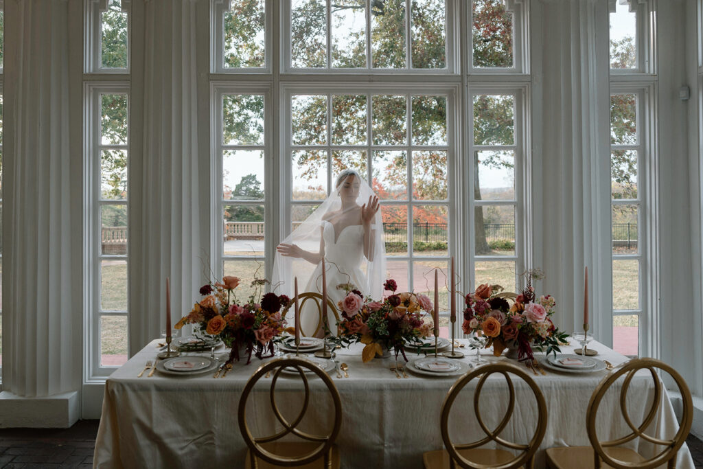 An editorial bridal portrait of the model bride in her luxury wedding gown from Stephanie's Bridal Boutique with the veil draped over her in front of the luxury design tablescape for this styled Longview Mansion wedding.