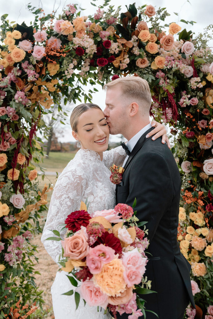 A romantic wedding portrait under a floral arch by Floriography KC in the Historic Sunken Garden at the Historic Longview Mansion.