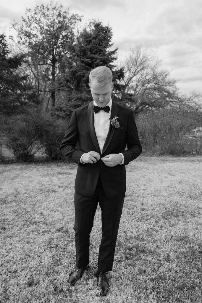 The groom buttons his suit jacket as he prepares for his wedding portraits at Longview Mansion.