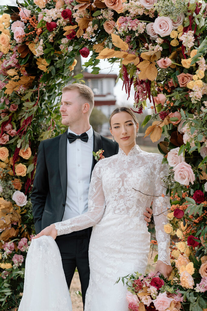 The model bride and groom take a picture under the Floriography KC floral arch for styled Kansas City wedding at Longview Mansion.