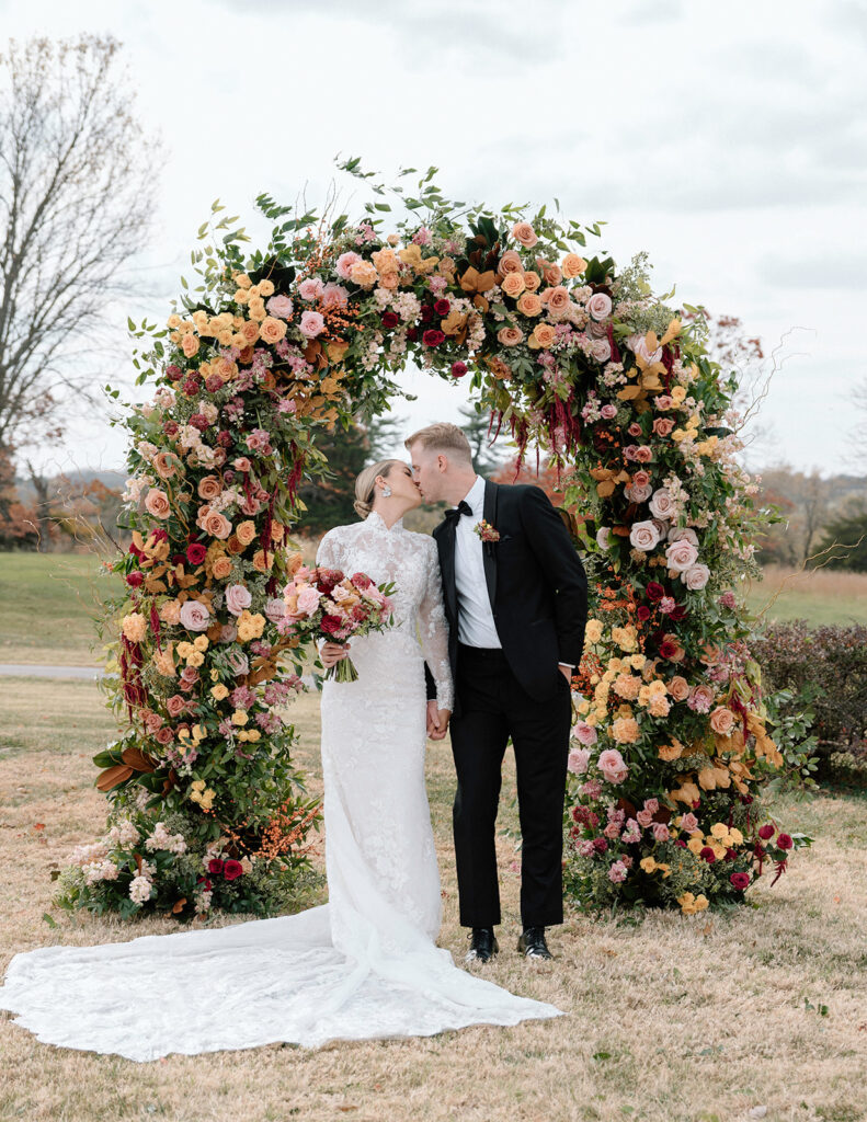 The models kiss under the floral arch from Floriography KC for the styled Longview Mansion wedding.