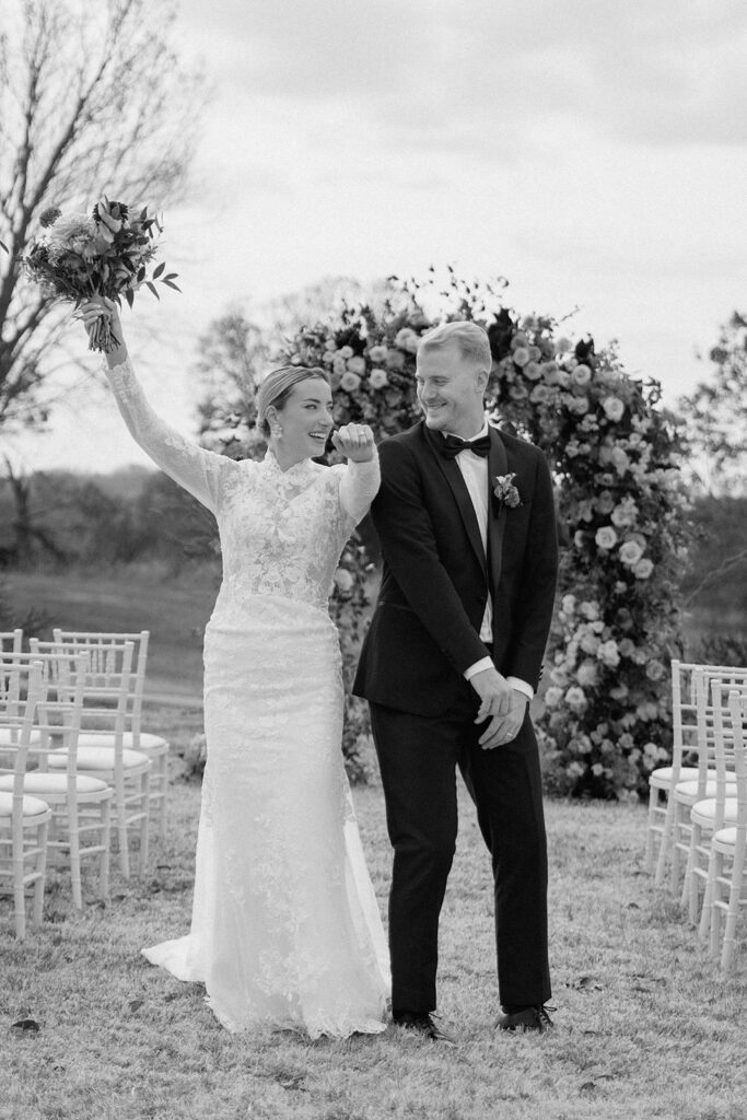 A black and white picture from a styled wedding at Longview Mansion in Kansas City of a bride and groom celebrating as they walk back down the aisle.